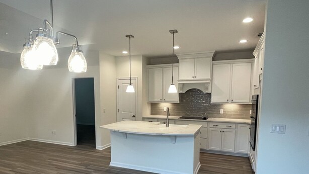 A modern kitchen with white cabinetry, a central island, and pendant lighting.