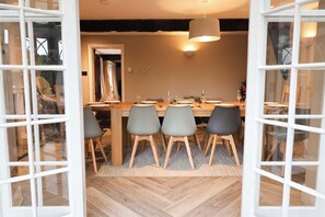 Un espace repas ouvert avec une table en bois, des chaises grises et un luminaire suspendu.