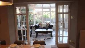 A dining area with a table set for four, a sofa in the background, and a view through a glass door to an outdoor seating area. - Habberjam Farm: Swimming Pool, Sauna, Hot Tub, Fire Pit (Marsh Lane)