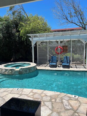 A swimming pool with a stone border, two lounge chairs, a covered seating area, and a lifebuoy.