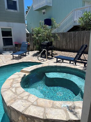 A backyard with a swimming pool, two lounge chairs, a barbecue grill, and a wooden fence.