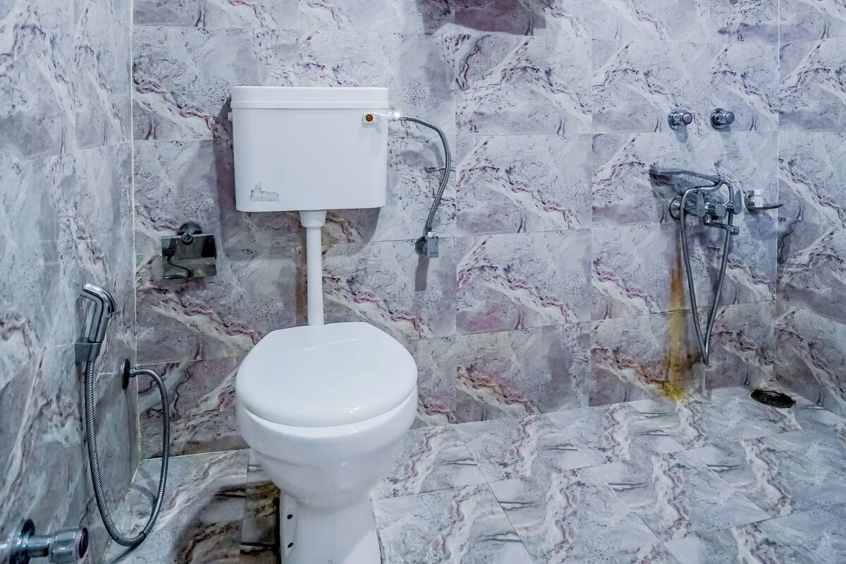 A bathroom with a marble floor, a white toilet, a shower, and a window.