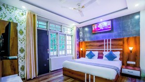 Un dormitorio con cama de madera, televisor montado en la pared, ventilador de techo y ventana con cortinas.