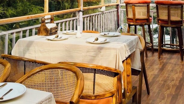 Un comedor cerrado con mesas y sillas, ventanas amplias y lámparas de mimbre colgantes.