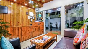 Zona de recepción con paneles de madera, mostrador de recepción, televisor y un área de estar con una mesa y sillas.