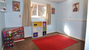 A child's playroom with a red carpet, shelves with toys, and superhero posters on the walls.