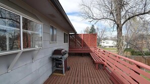 A deck with a barbecue grill and a wooden bench.