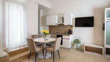 A modern kitchen with white cabinets, a built-in stove, and a flat-screen TV mounted above the counter.