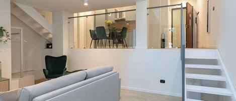 A modern living room with a grey sofa, a dining area with chairs and a table, and a staircase.