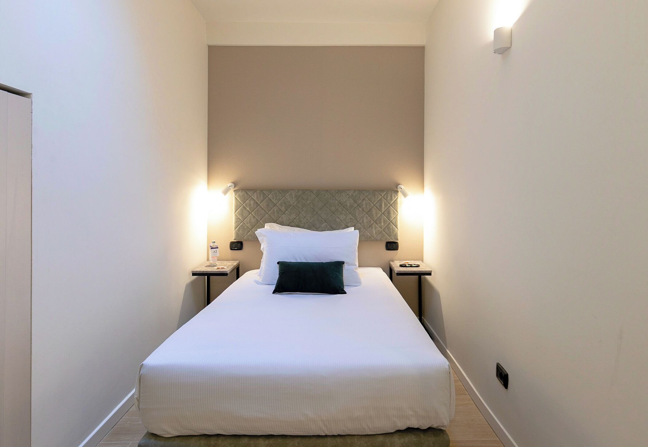 A hotel room with a large bed, two bedside tables, and a headboard with integrated lighting.