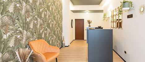 Un pasillo con mostrador de recepción, piso de madera y un mural de plantas tropicales en la pared.