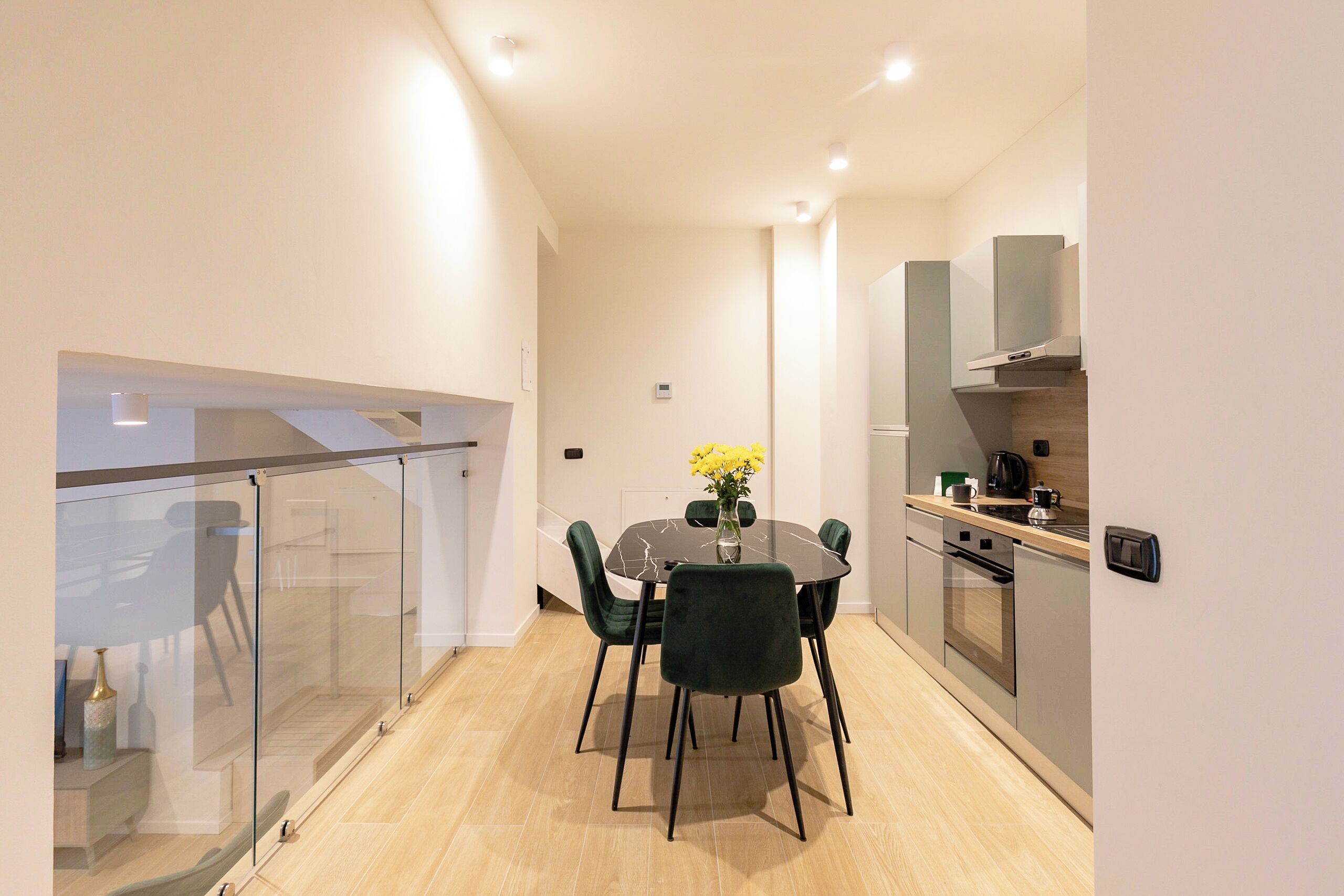 A modern kitchen with a dining area, featuring a glass railing, a round table with chairs, and a built-in oven.