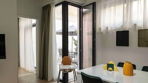 A dining area with a table, chairs, a high chair, and a window with curtains.