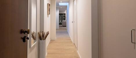 A hallway with a wooden floor, white walls, and a white vase with dried plants.