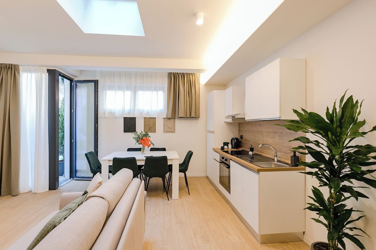 A modern apartment with a dining area, kitchenette, and a large window with curtains.