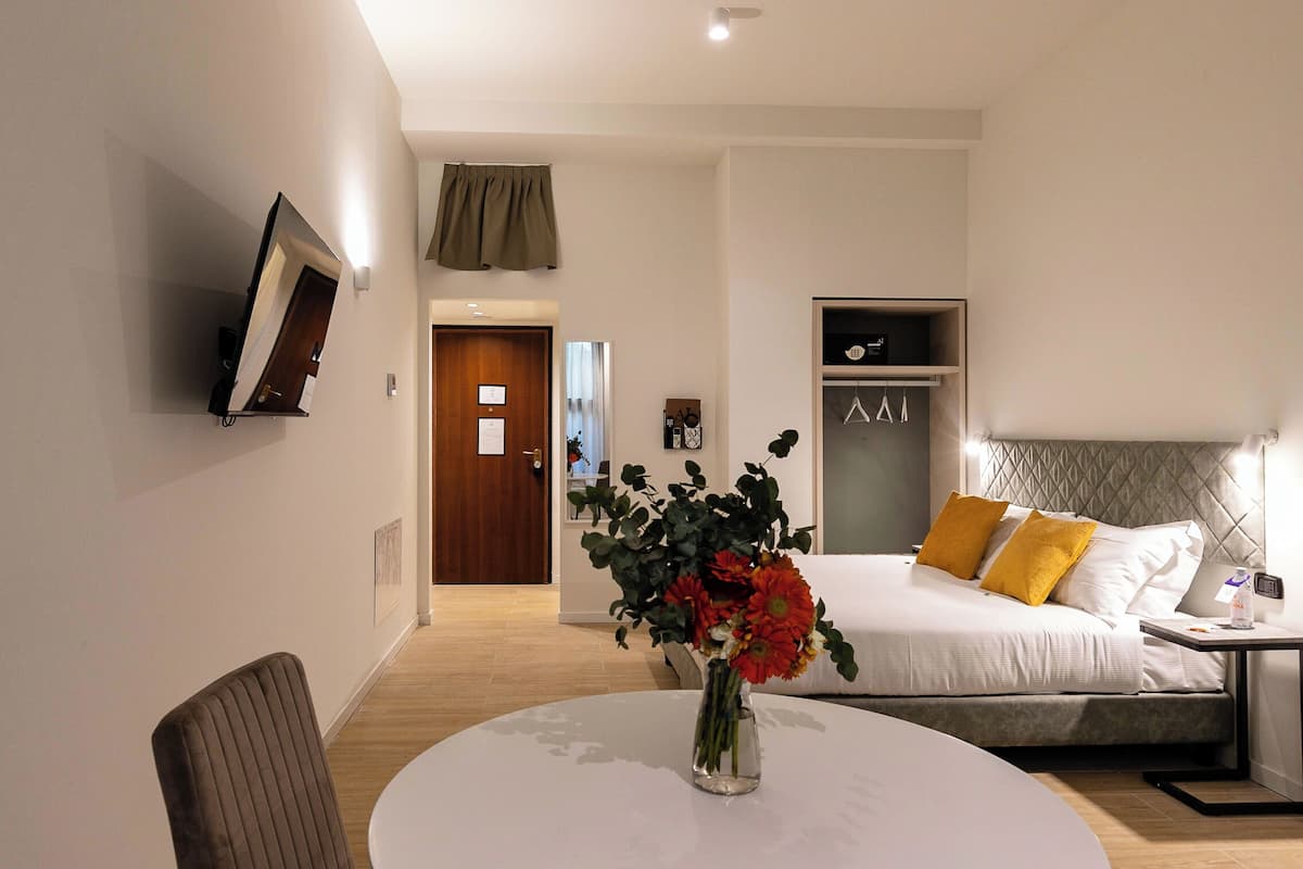 A modern hotel room with a bed, bedside table, and a small table with a vase of flowers.