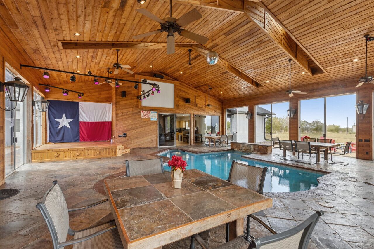 Un vaste espace intérieur abritant une piscine, avec un plafond en bois, un drapeau et une table entourée de chaises.