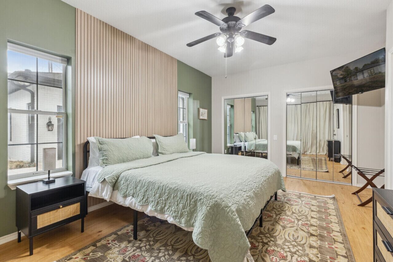 A bedroom with a bed, a ceiling fan, a TV, and a window.