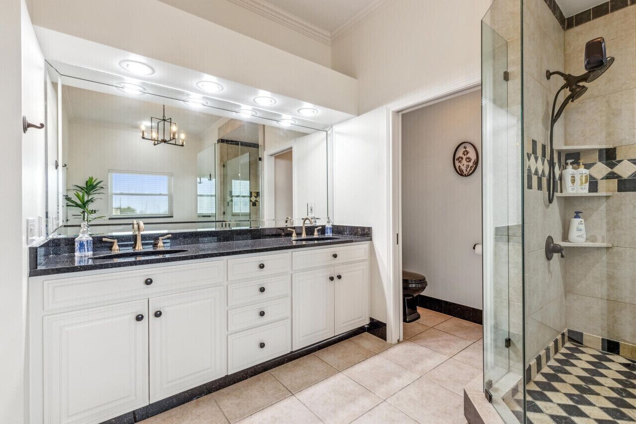 A modern bathroom with a large vanity, a glass shower enclosure, and a mirror with lights.