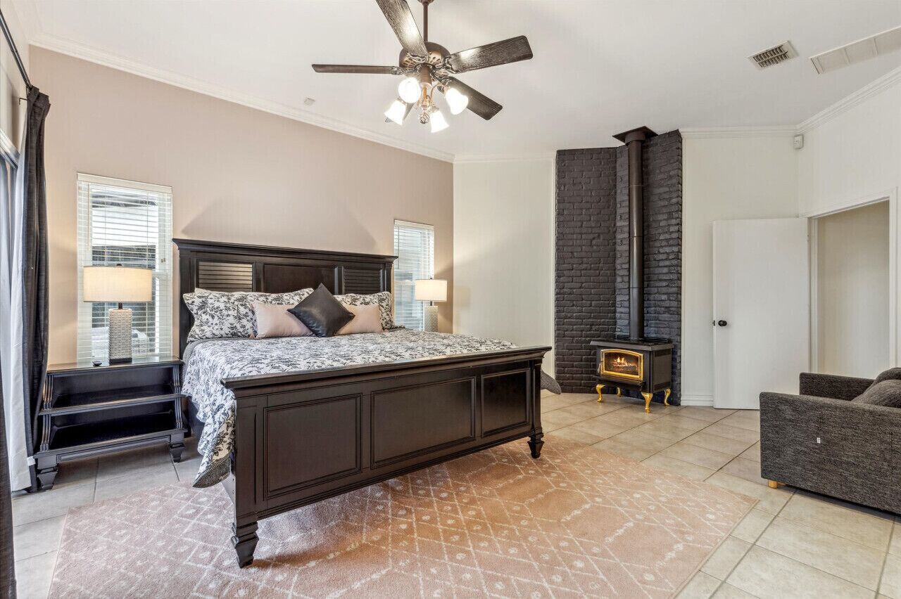 A bedroom with a large bed, a dark wood headboard, a fireplace, a ceiling fan, and a dark-colored sofa.