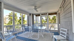 A covered patio with a table and chairs, a ceiling fan, and large windows offering views of the neighborhood.