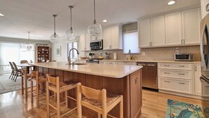 A spacious kitchen with a central island, wooden bar stools, white cabinetry, and modern appliances.