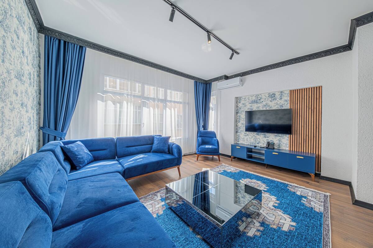 A modern living room with a sectional sofa, a glass coffee table, and a blue patterned rug.