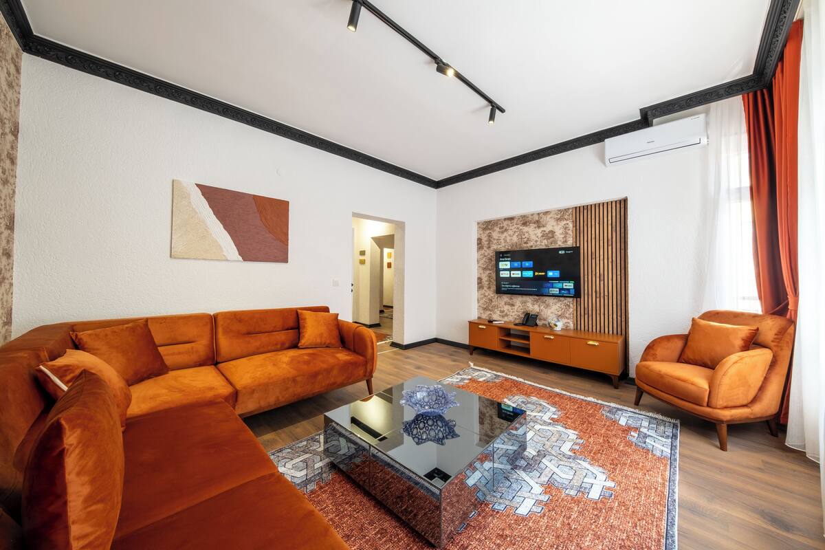 A modern living room with a sectional sofa, a glass coffee table, and a flat-screen TV mounted on the wall.