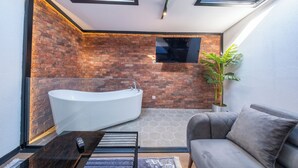 A modern bathroom with a freestanding bathtub, a grey sofa, and a potted plant. - Hexa Apartments Sisli  (Istanbul)