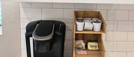 Una cocina con cafetera, estantes con vajilla y un depósito para granos de café.