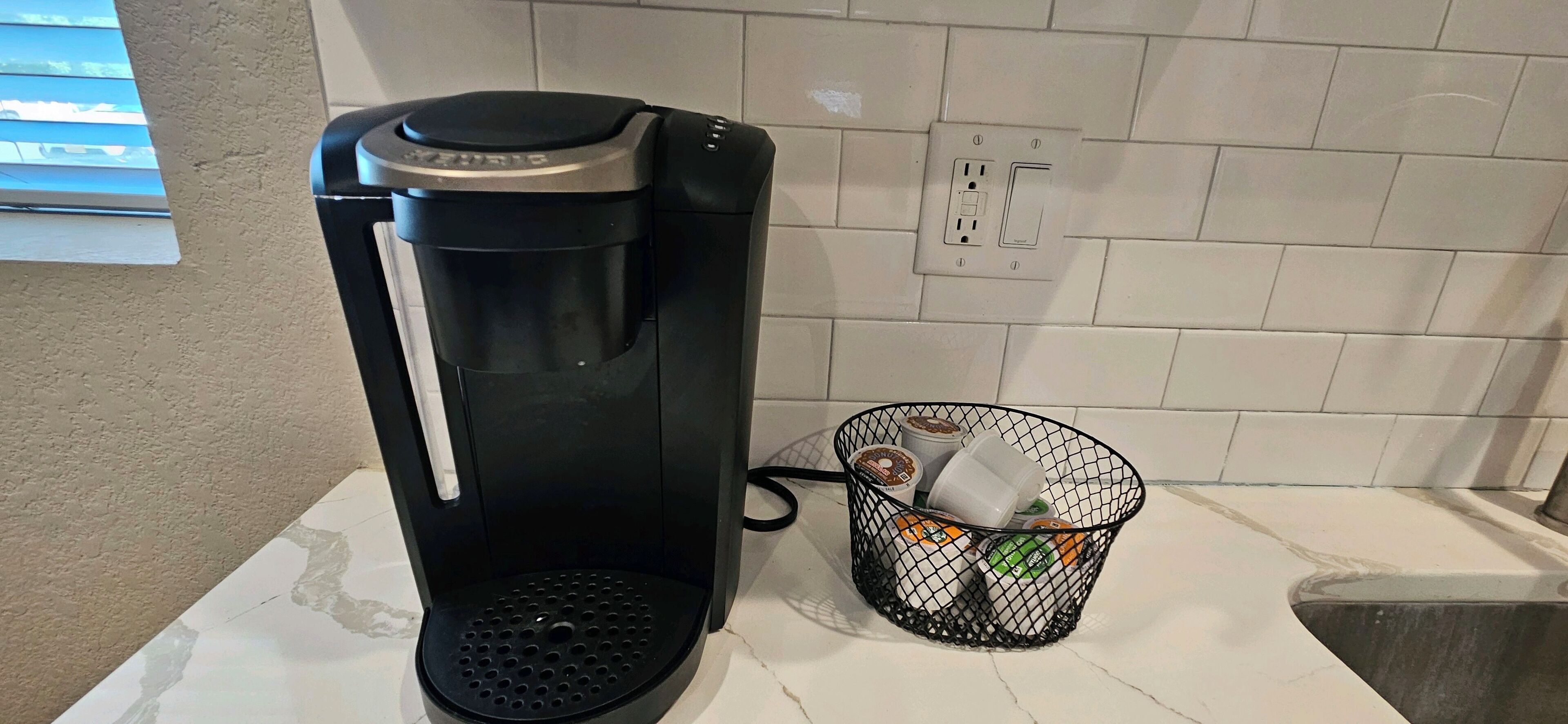 A coffee maker on a kitchen counter next to a basket with coffee pods and a coffee grinder.