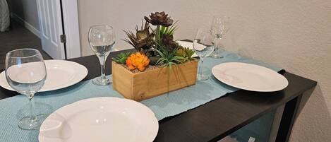 A dining table with two white plates, two wine glasses, and a wooden planter box with succulents.