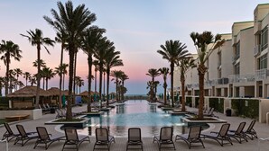 A poolside area with lounge chairs, palm trees, and a building with balconies. - Sapphire Condo & Spa Unit # 2106 3 Bedroom Condo (South Padre Island)
