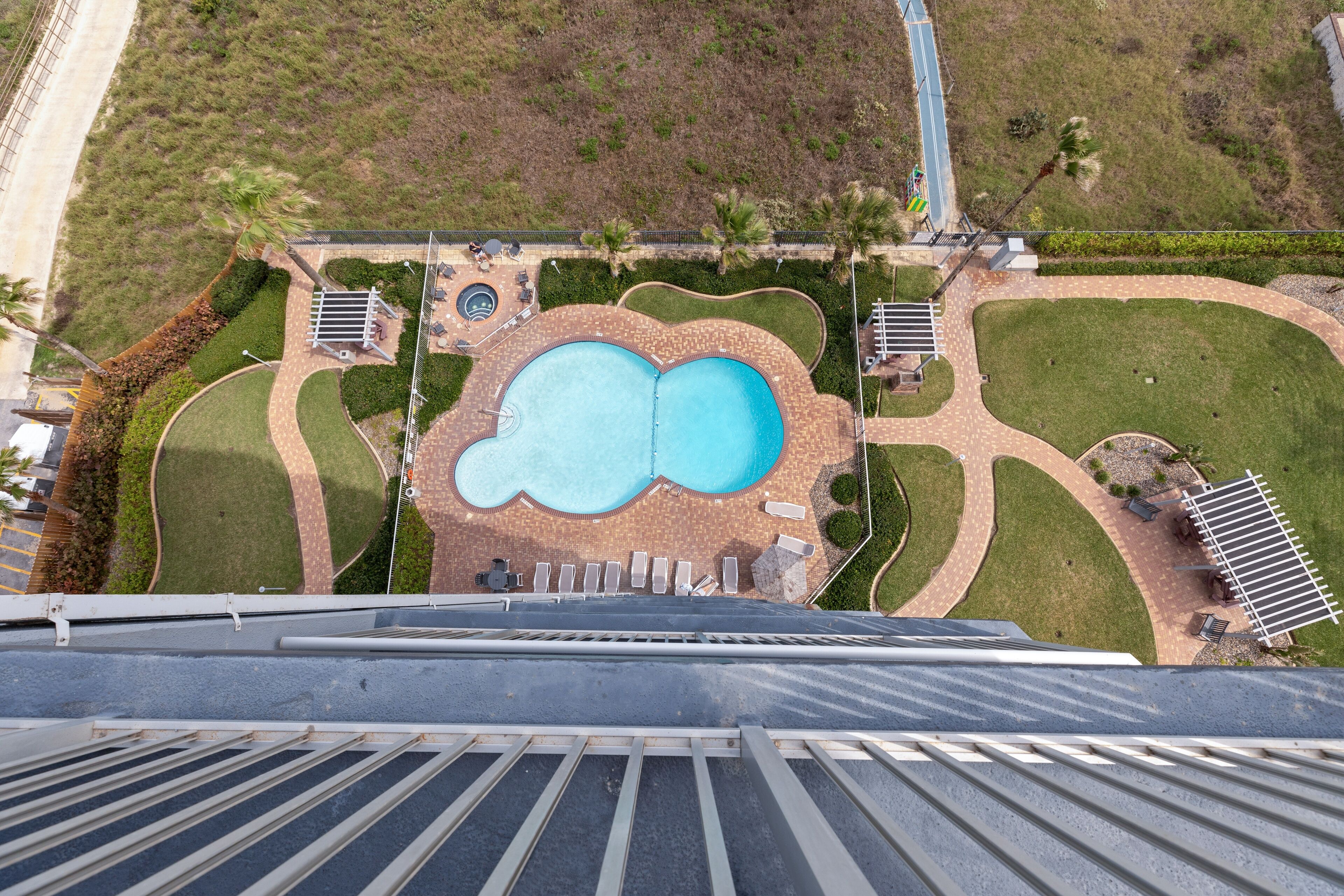 An aerial view of a resort with a large swimming pool, landscaped gardens, and a parking area.