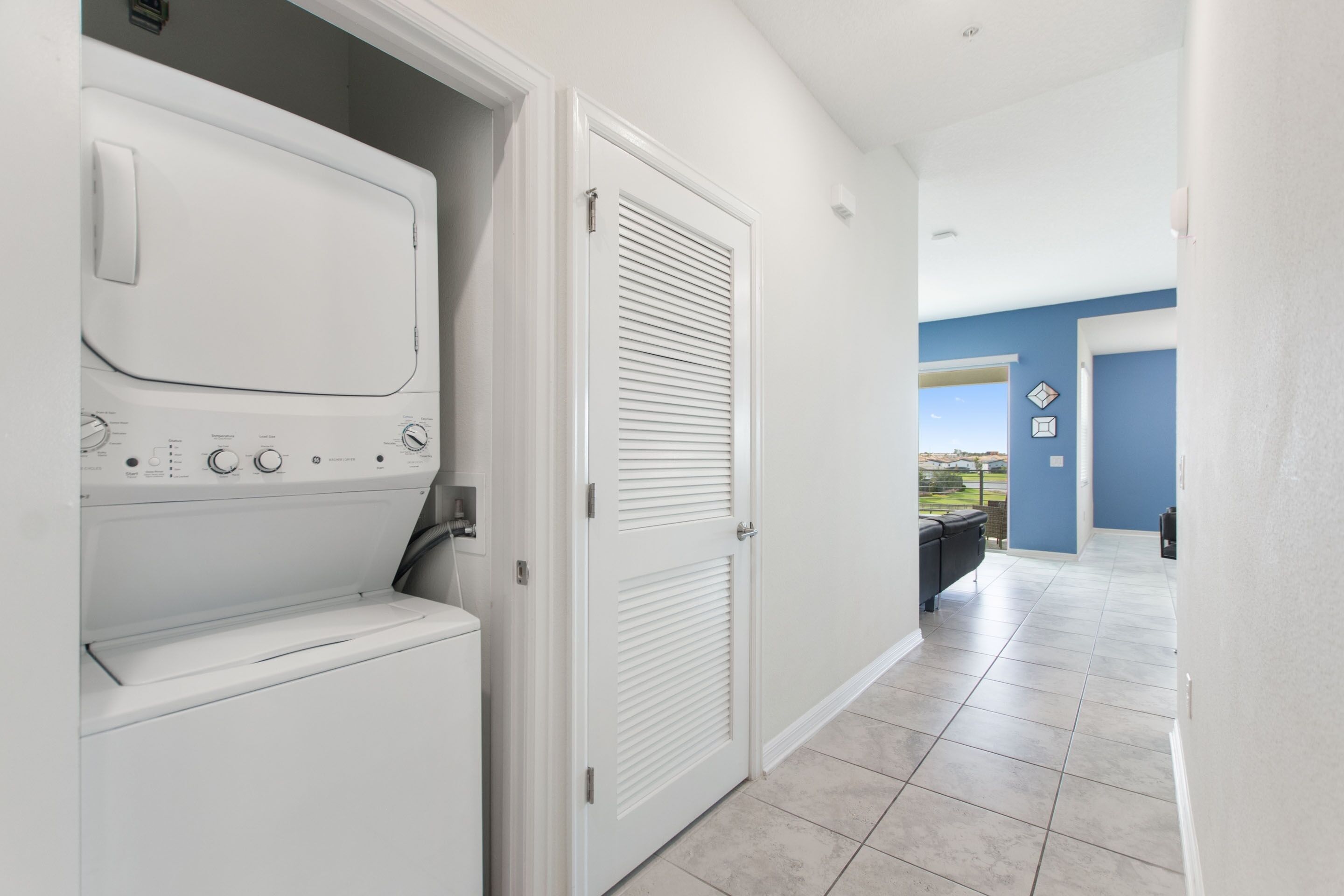 A laundry room with a washer and dryer, a closed door, and a view of a balcony with outdoor scenery.
