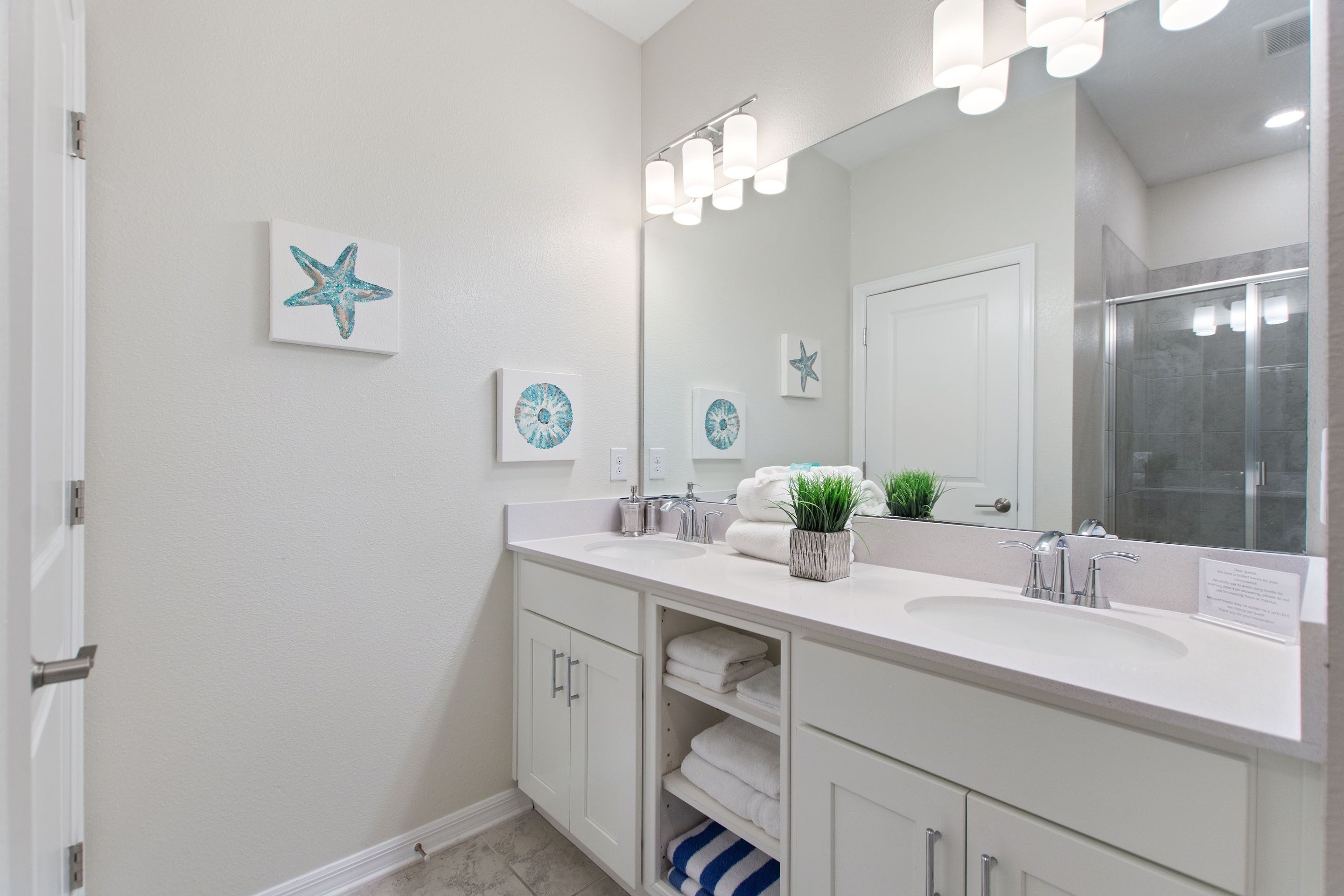 A modern bathroom with a white vanity, two sinks, a large mirror, and decorative starfish wall art.