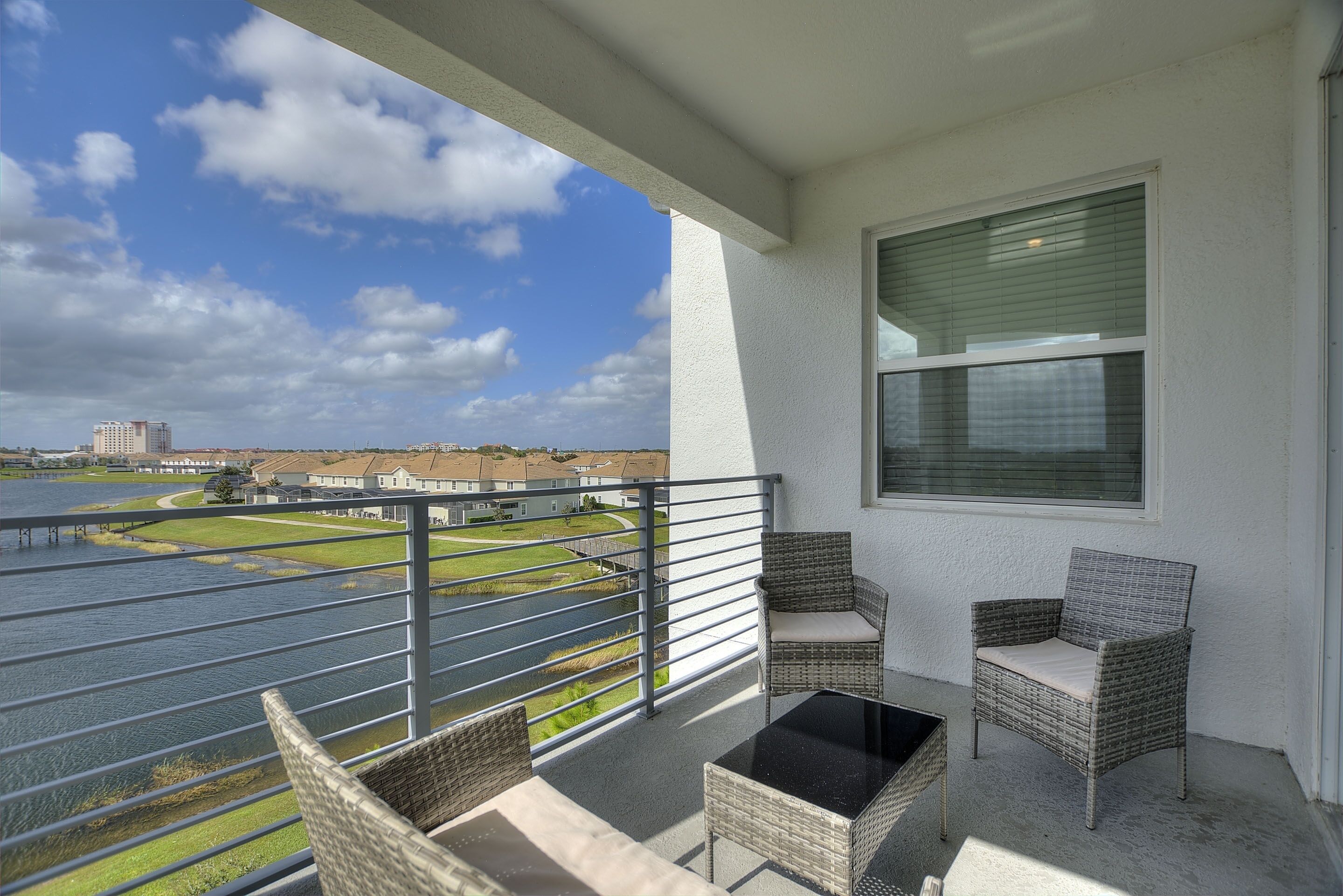 A balcony with wicker furniture, a view of a body of water, and a building in the background.