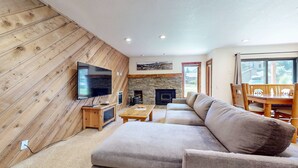 Ein gemütliches Wohnzimmer mit Kamin aus Stein, Holzwänden, einem Flachbildfernseher, einer Couch und einem Esstisch.