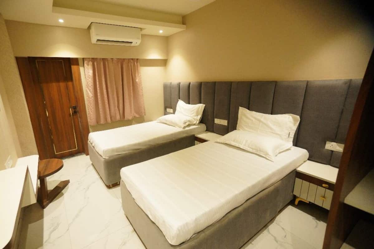 A hotel room with two single beds, a small desk, a chair, and a window with curtains.