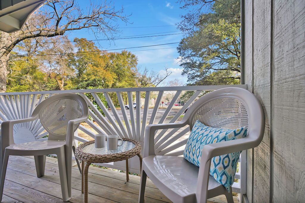 A covered outdoor seating area with two white plastic chairs and a small round table, featuring a woven chair base.