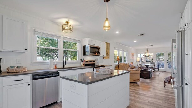 Een moderne keuken met witte kasten, een centraal kookeiland en een eethoek met een bank en tafel.