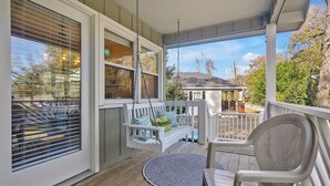 Een veranda met een schommel, een stoel en een uitzicht op een huis op de achtergrond.