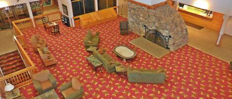 Un vestíbulo amplio con alfombra roja, varias zonas de estar, una chimenea de piedra y un reloj en la pared.