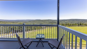 Ein überdachter Balkon mit zwei Korbstühlen und einem kleinen Tisch, mit Blick auf eine grüne Landschaft mit Hügeln.