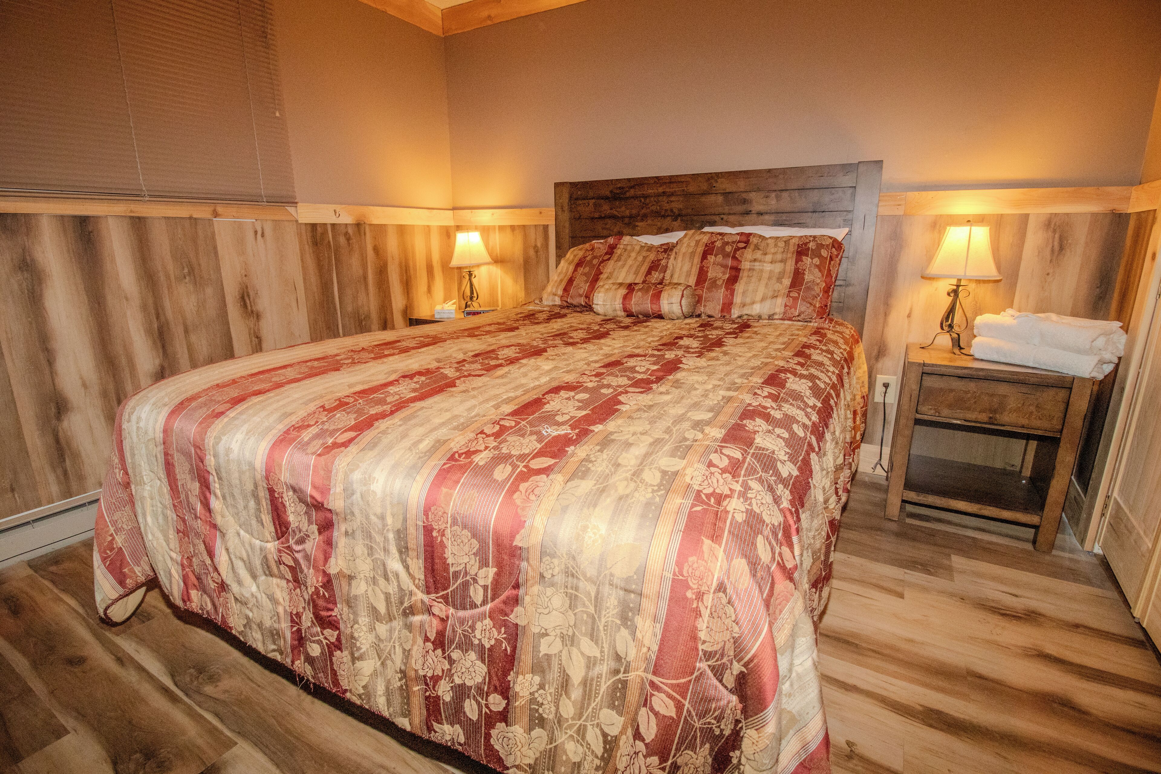 Een slaapkamer met een groot bed, een houten hoofdbord, twee nachtkastjes met lampen en een houten vloer.