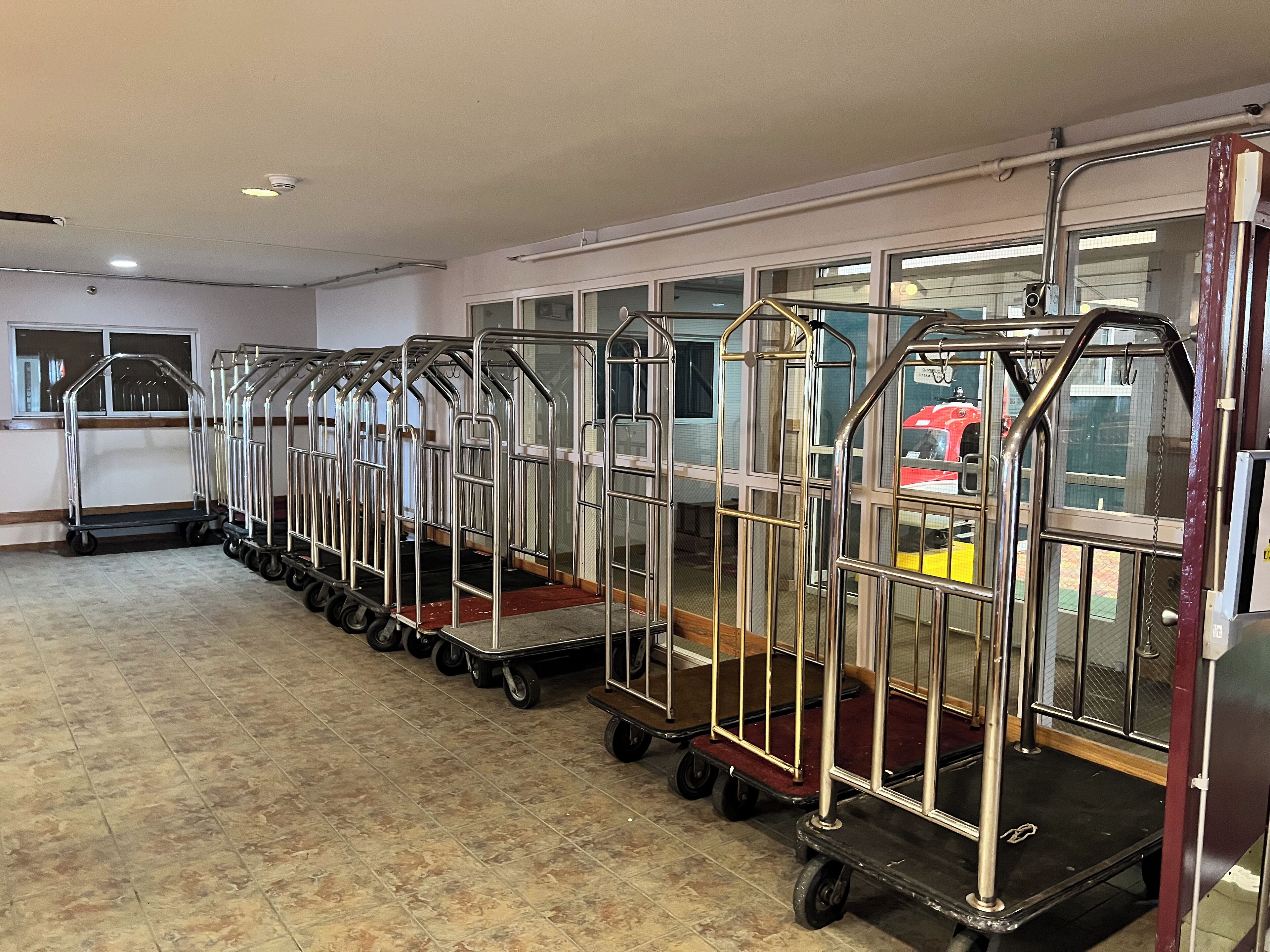 Une rangée de chariots de service en métal se trouve dans une pièce dont le sol est carrelé et qui possède de grandes fenêtres.