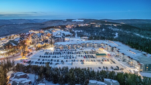 Ein schneebedecktes Resort mit mehreren Gebäuden, einem Parkplatz und bewaldeten Hügeln im Hintergrund.