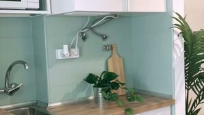 Une cuisine avec des meubles blancs, un évier en acier inoxydable, un four à micro-ondes et une planche à découper en bois.