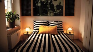 A bedroom with a striped bed, two bedside lamps, a potted plant, and a framed picture on the wall.