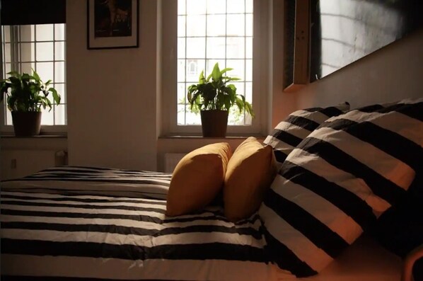 Una cama con ropa de cama a rayas, dos plantas en macetas y una ventana con vistas.